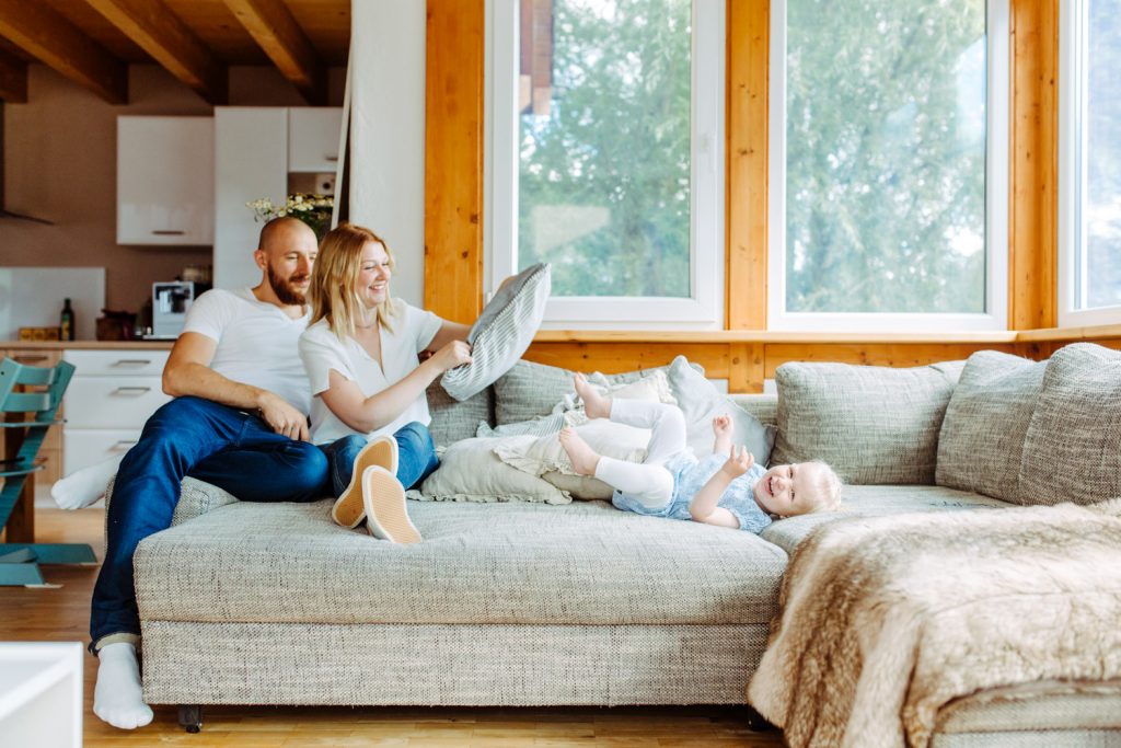Mutter und Vater mit Kind toben auf dem Sofa