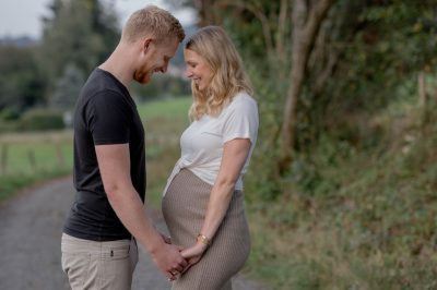 Schwangere Frau und Mann halten Händchen und lachen.